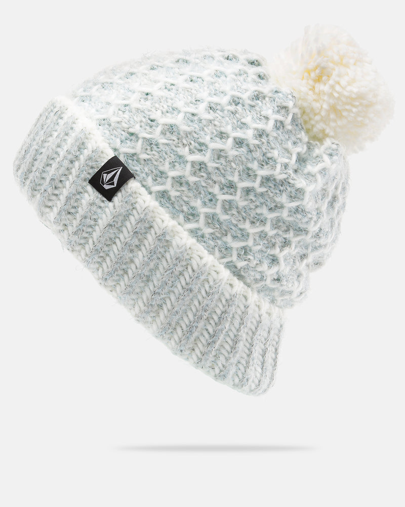 The Women’s Frosty Top Beanie by Volcom features a white and light blue knitted design with a large faux fur pom on top and a folded brim. A small black patch with the Volcom logo appears on the cuff. The beanie is displayed against a plain white background.