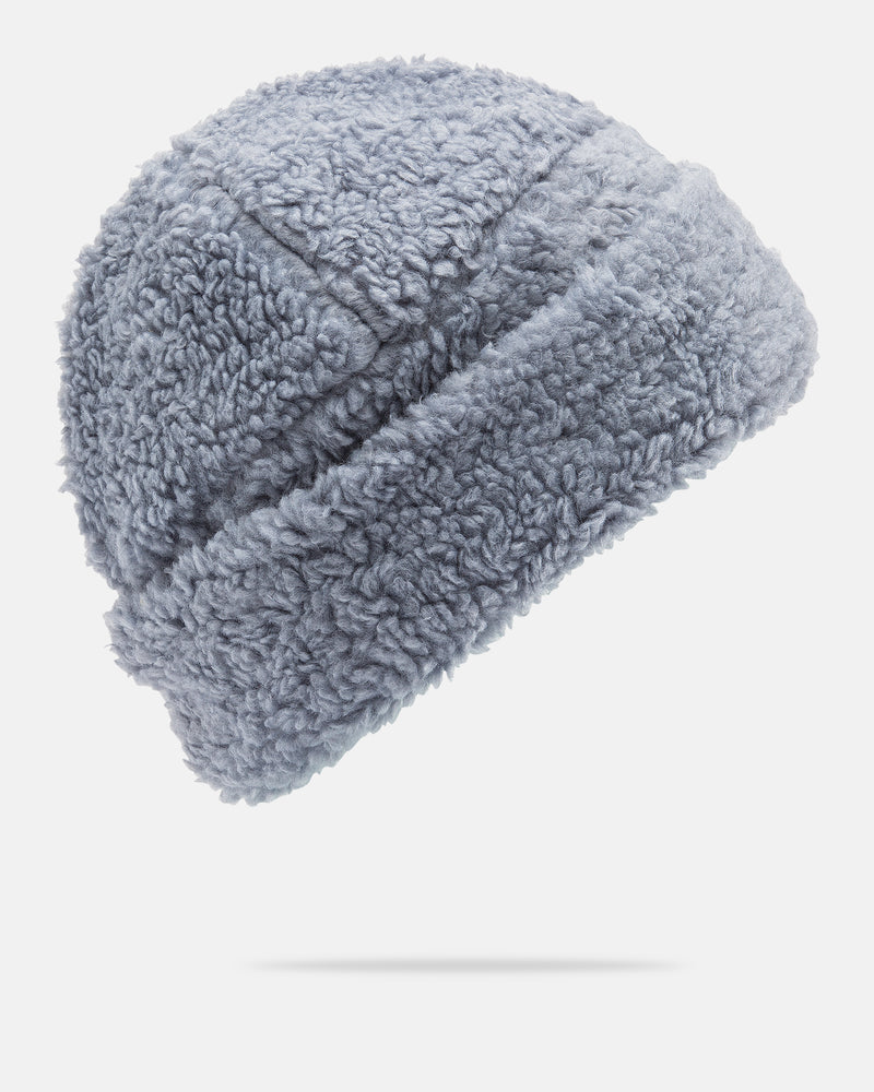 The Volcom Women’s Fuzzed Up Beanie is a soft, fleece-lined women’s hat in light gray, featuring a classic fit and a textured, curly pattern, displayed against a plain white background.