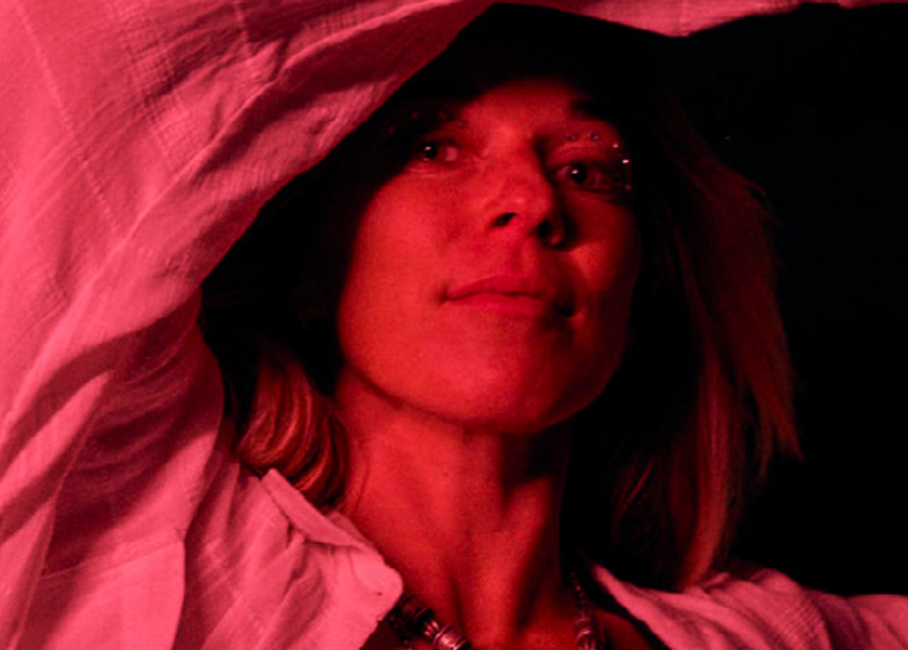 Person with red lighting and a pinkish hue, wearing a light-colored garment.