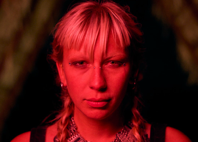 Person with pink hair and red lighting in a dark setting