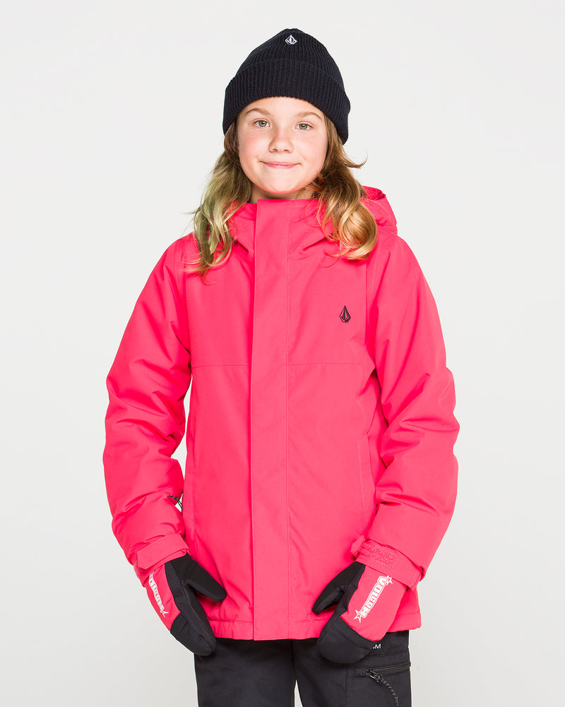 A child wearing the Volcom Kids’ Sass’N’Frass Insulated Jacket in bright pink, featuring a helmet-compatible hood, stands against a plain white background with a black beanie and black gloves, smiling slightly at the camera.