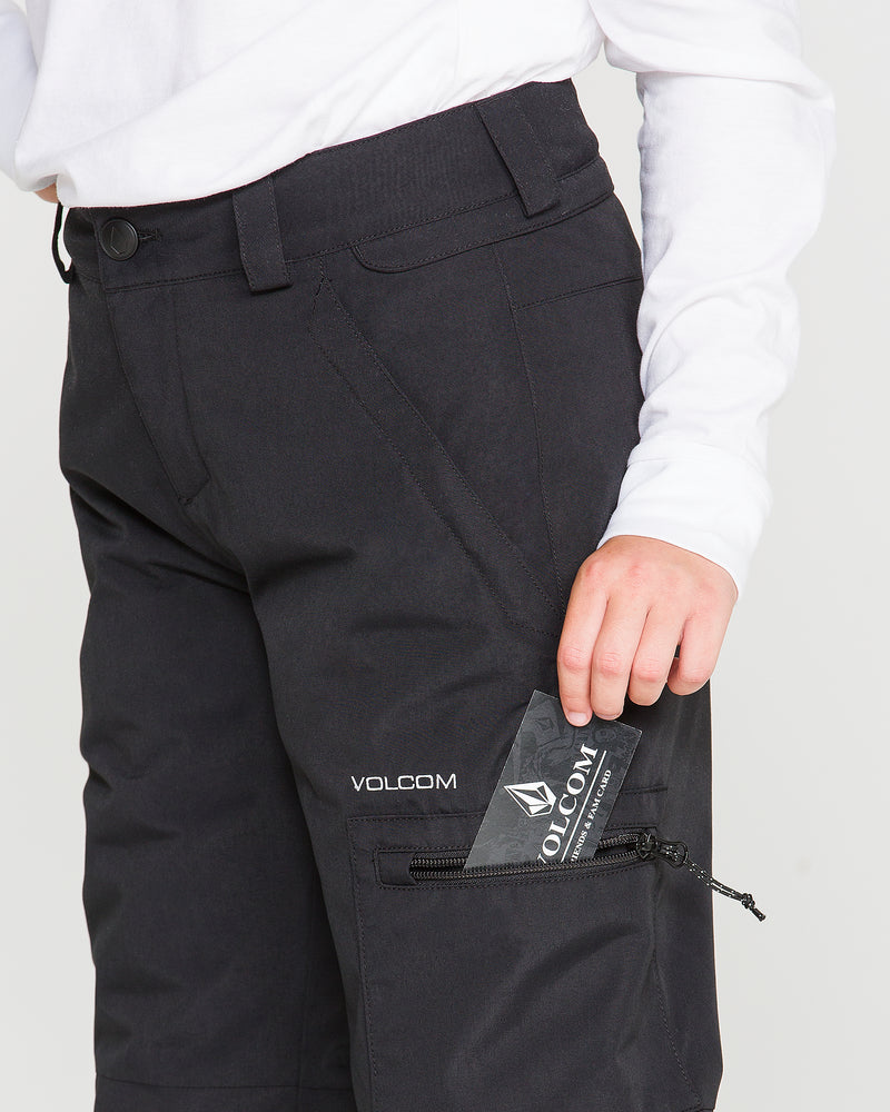 A person wearing black Volcom Kids’ Frostique Insulated Pants with an adjustable waist and a white long-sleeve shirt puts a Volcom card into a zippered pocket on their pants.
