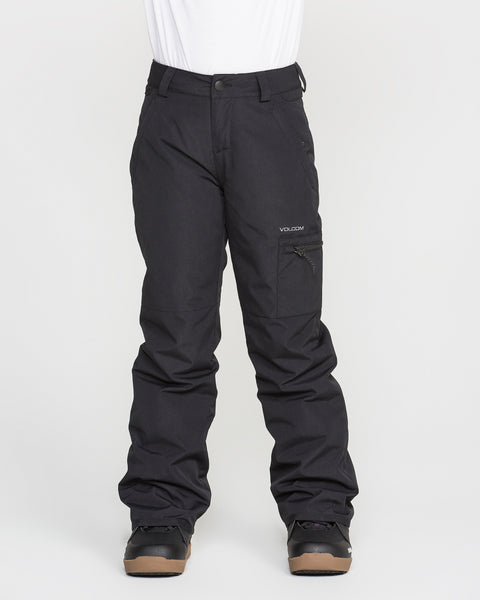 A person is wearing black Volcom Kids’ Frostique Insulated Pants with recycled insulation and black boots, standing against a plain white background. These pants feature an adjustable waist, a zippered pocket on the right thigh, and belt loops at the waist.