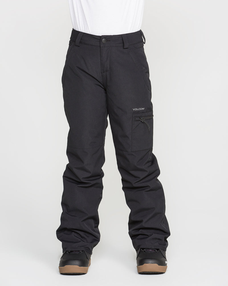 A person is wearing black Volcom Kids’ Frostique Insulated Pants with recycled insulation and black boots, standing against a plain white background. These pants feature an adjustable waist, a zippered pocket on the right thigh, and belt loops at the waist.