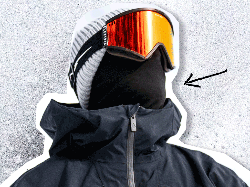 A person wearing a black jacket, a gray knit beanie, orange ski goggles, and a black face covering that completely hides their face. There is a black arrow pointing to their covered face.