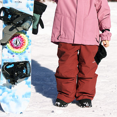 Person wearing pink jacket and red pants standing on snow with a colorful snowboard in the foreground.