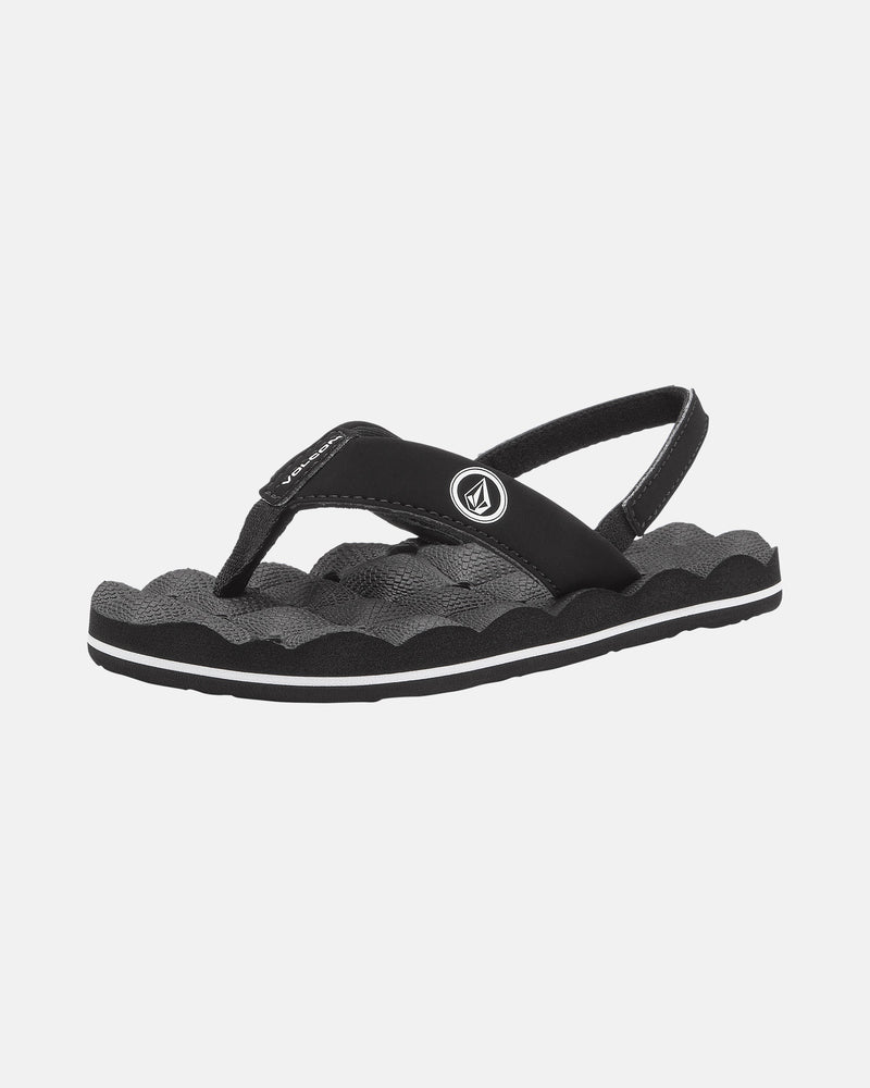 The Volcom Kids' Recliner 2 Little Youth sandal features black and gray colors, a textured wavy sole, thong and back heel straps, a comfort foam footbed, and a circular white logo on the side. Displayed on a plain white background.