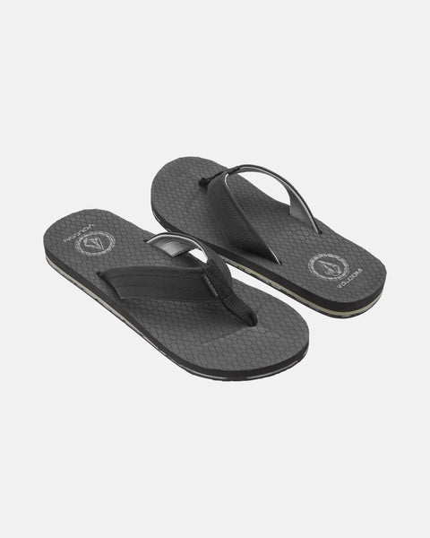 A pair of Men's Vol-Commuter Sandals by Volcom with black textured soles, black straps, a subtle geometric pattern, and a circular logo near the heel, shown on a white background.