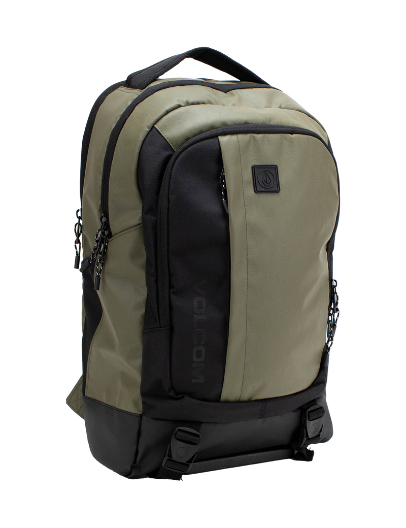 Introducing the Volcom Men's Venture Backpack in khaki and black, featuring a spacious 22L capacity with a front pocket, two side zippers, top handle, and a prominent black Volcom logo patch on the front. It includes a padded laptop sleeve for extra protection, a reinforced base for durability, and two bottom straps with buckles for added functionality.