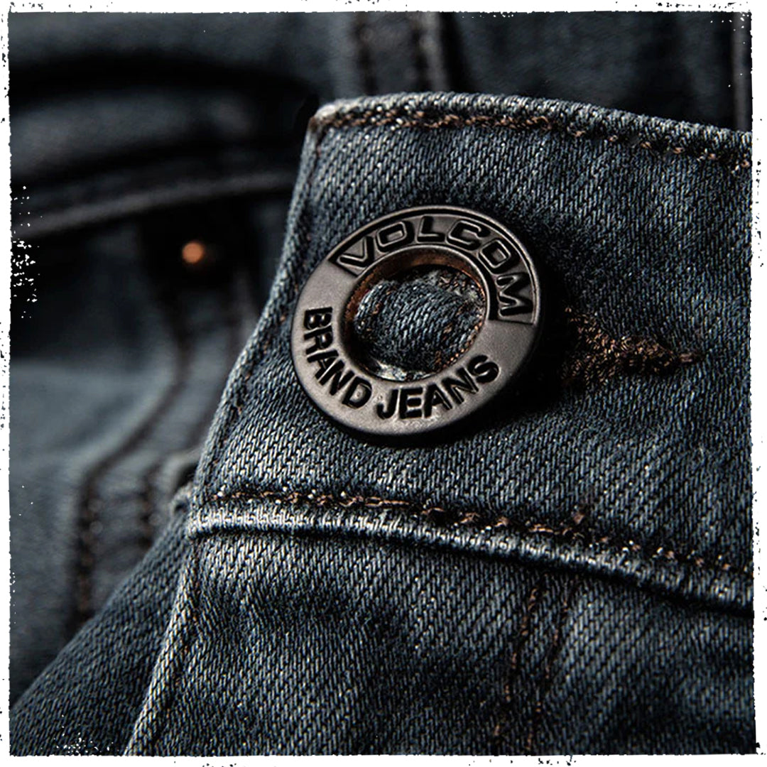 Close-up of a dark blue denim jacket showing the Volcom Brand Jeans metal button and textured denim fabric.