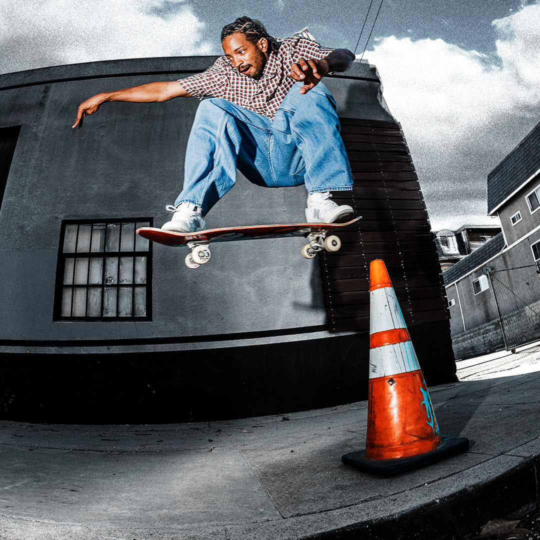 Person doing skateboard trick over traffic cone outside