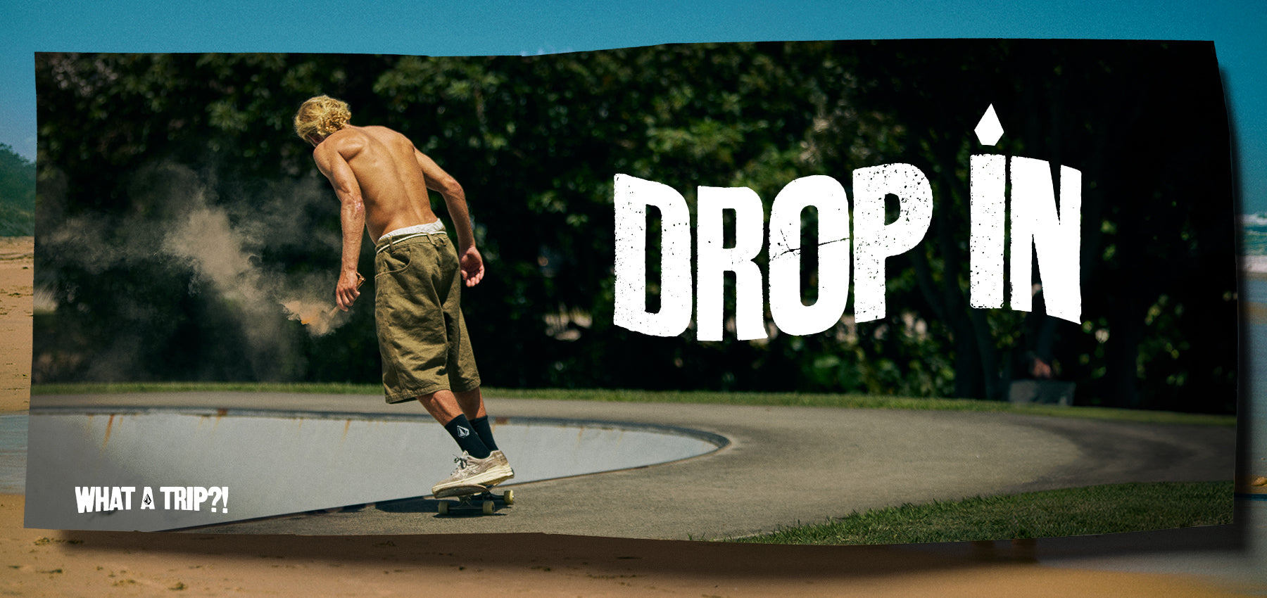 Shirtless skateboarder riding along the edge of a concrete bowl in a wooded area, kicking up dust; large text reads ‘Drop In’ 