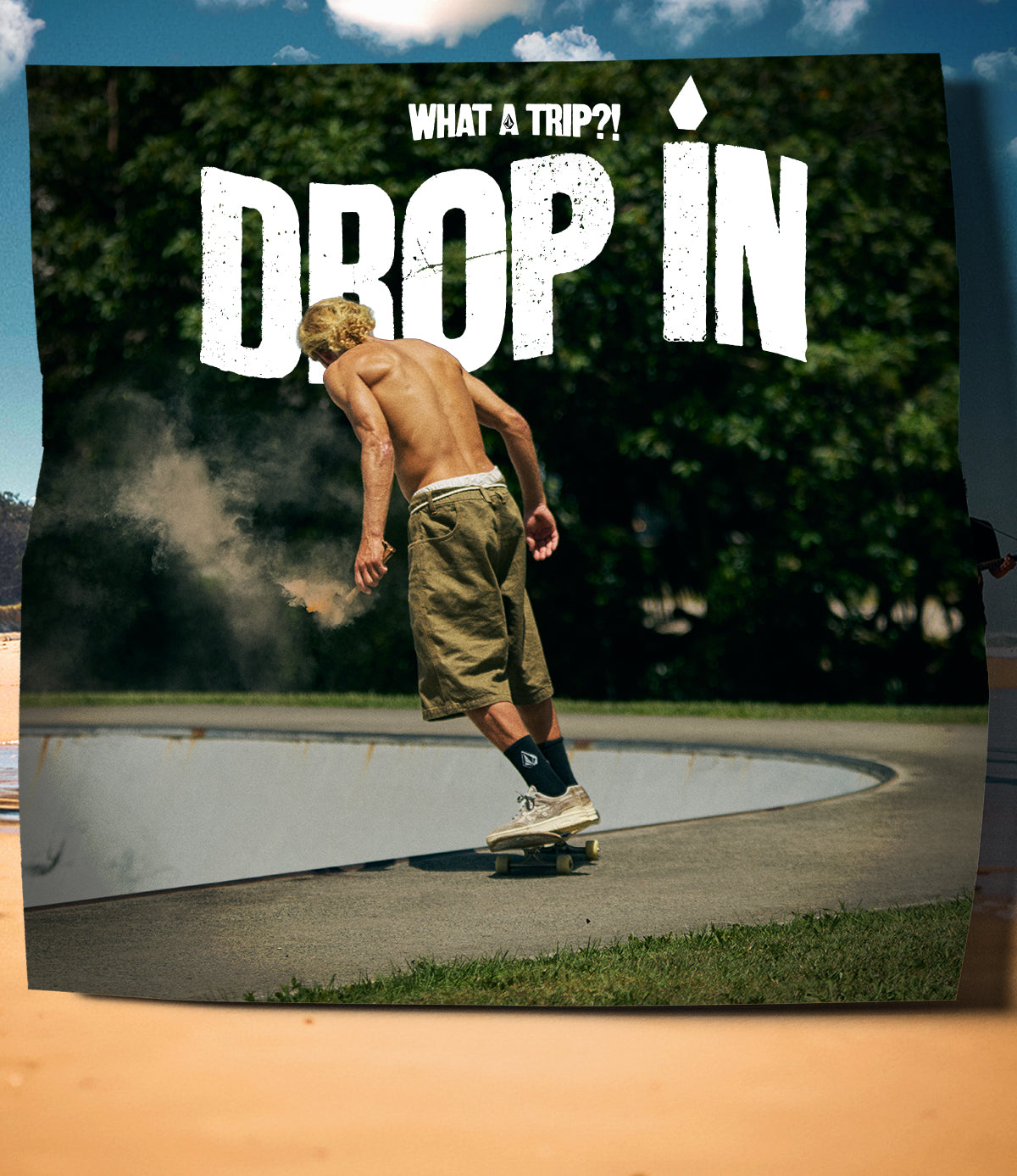Shirtless skateboarder riding along the edge of a concrete bowl in a wooded area, kicking up dust; large text reads ‘Drop In’