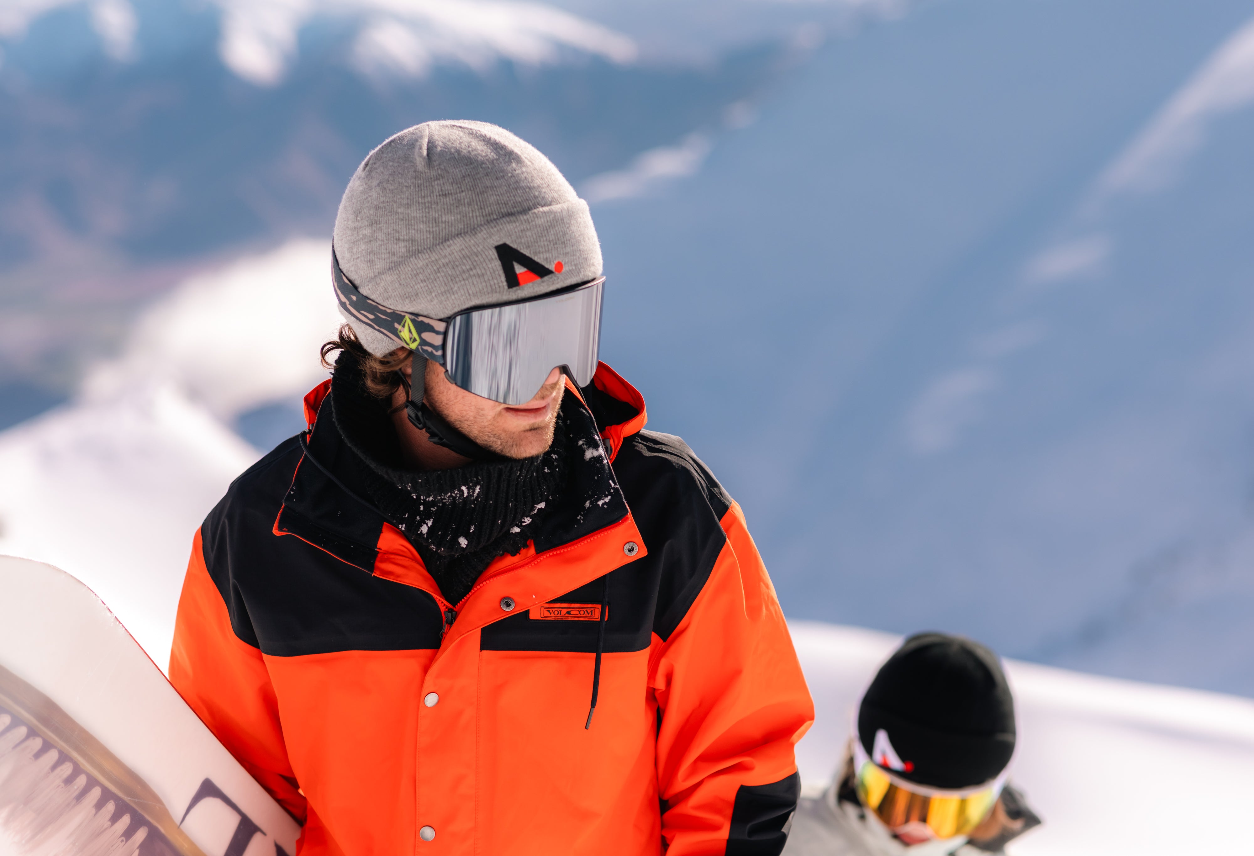 Person in orange jacket and gray helmet with goggles on a snowy mountain background