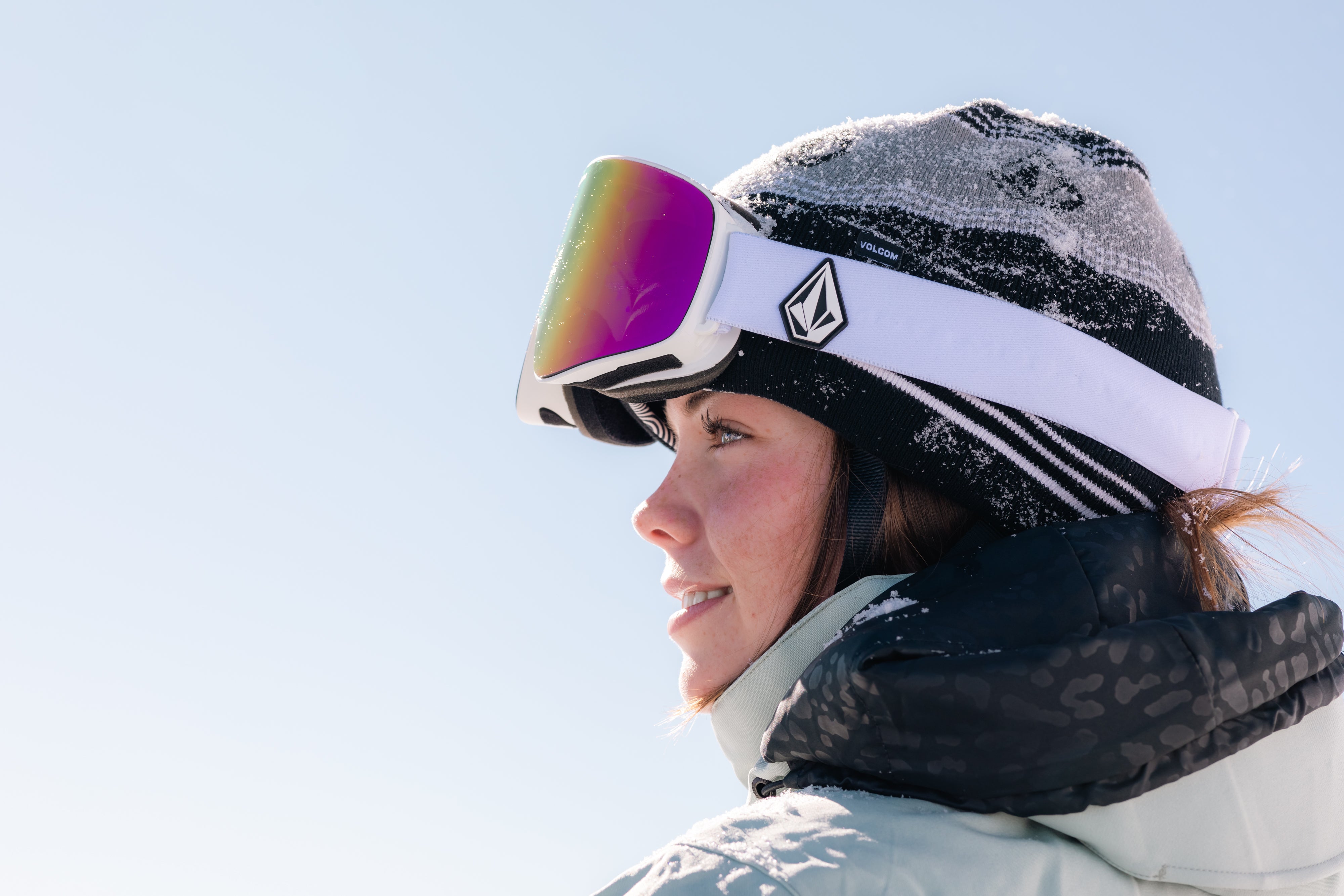 Person wearing a helmet with goggles and a light-colored jacket against a clear blue sky.