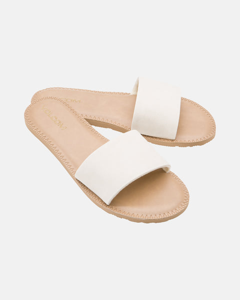 The Volcom Women's Simple Slide features beige flat sandals with wide white straps and tan soles, shown on a white background.