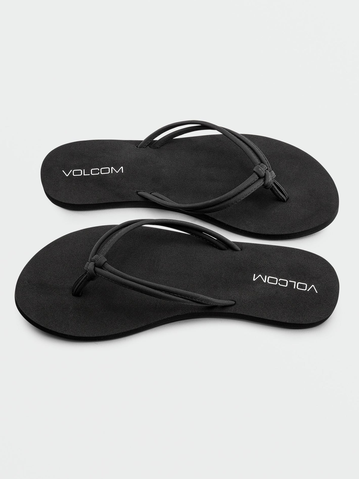 A pair of Volcom Women's Forever And Ever II black flip-flops, featuring thin synthetic leather straps and "VOLCOM" printed in white on the footbeds, with molded arch support for added comfort, displayed on a white background.