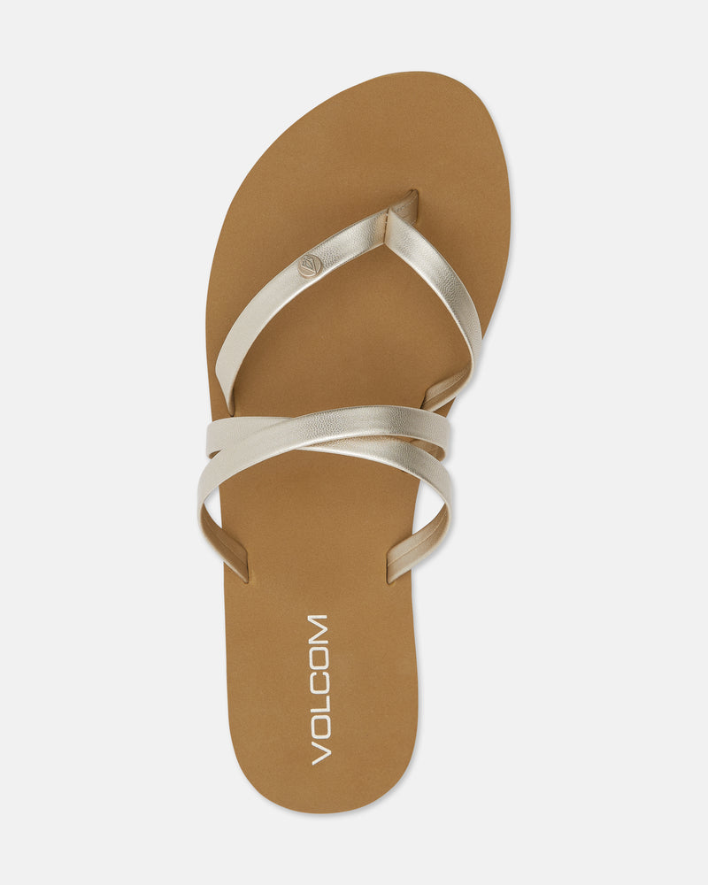 The Easy Breezy II sandal features brown flat strappy design with metallic beige crisscross straps and "VOLCOM" in white on the insole. Its minimalist style includes an EVA footbed for comfort.