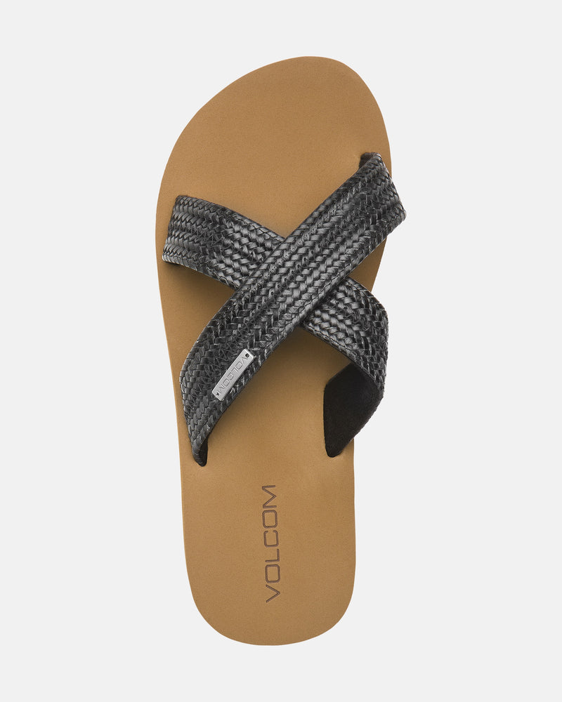 The Women's Volcom Double Cross Sandal by Volcom features a tan footbed with VOLCOM near the heel and two overlapping black textured straps forming an X across the top.