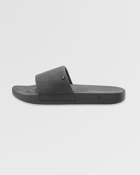 The Women's Volcation Slides by Volcom are black slide sandals featuring a wide single strap and flat sole for everyday comfort, ideal for summer wear. Shown against a white background.