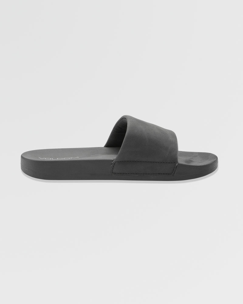 The Women's Volcation Slides by Volcom are black summer sandals with a wide single strap and flat sole, delivering everyday comfort and signature style. Shown in side profile on a plain white background.