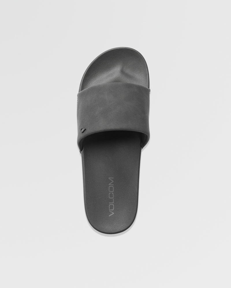 A single black Women's Volcation Slide by Volcom, featuring a wide strap and flat sole, is shown from above on a plain white background. The footbed displays the Volcom logo, highlighting its everyday comfort design.