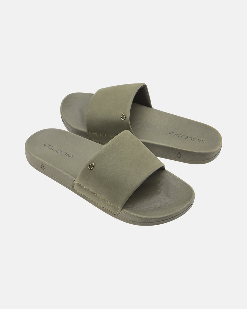 The Women's Volcom Volcation Slides feature olive green wide straps and flat soles, offering everyday comfort and classic Volcom style, shown against a white background.