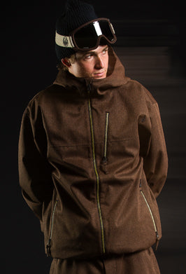 A man wearing a brown hooded ski jacket, a black knit beanie, and ski goggles, posed against a dark studio background.