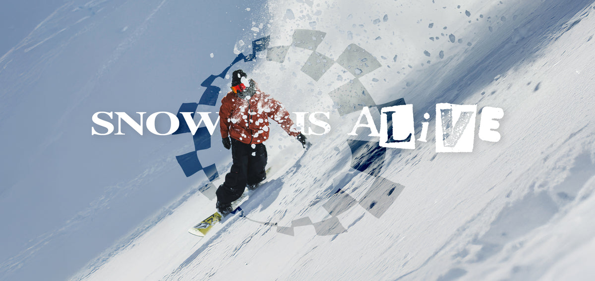 A snowboarder in a red and black jacket rides down a snowy mountain slope, with large white text reading 'SNOW IS ALIVE' overlaid across the scene.