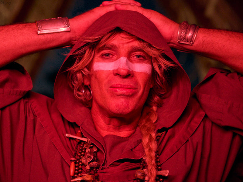 Person wearing a red outfit with a hood, sitting with hands on head.