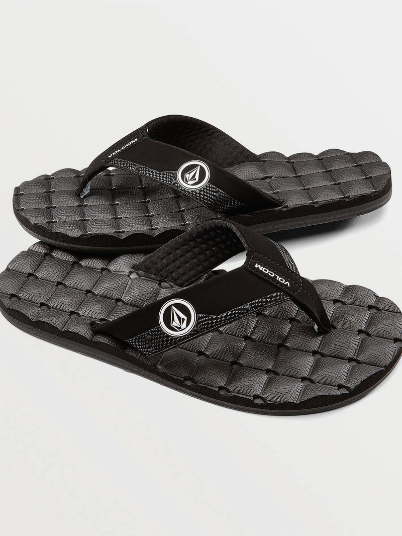 A pair of black Volcom Kids' Big Recliner Sandals with textured, square-patterned soles and wide straps featuring the white Volcom logo are displayed on a plain white background. These sandals are water-friendly.