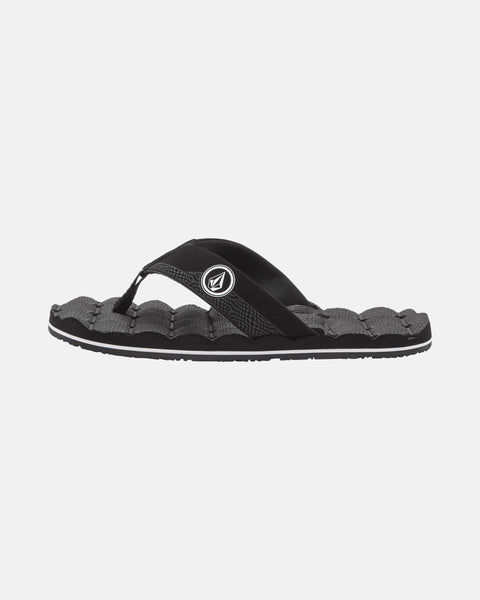 The Volcom Kids' Recliner 2 Big Youth sandal features a black and gray design with a textured sole, black strap with white circular logo, and comfort foam footbed for cushioning, shown on a plain white background.