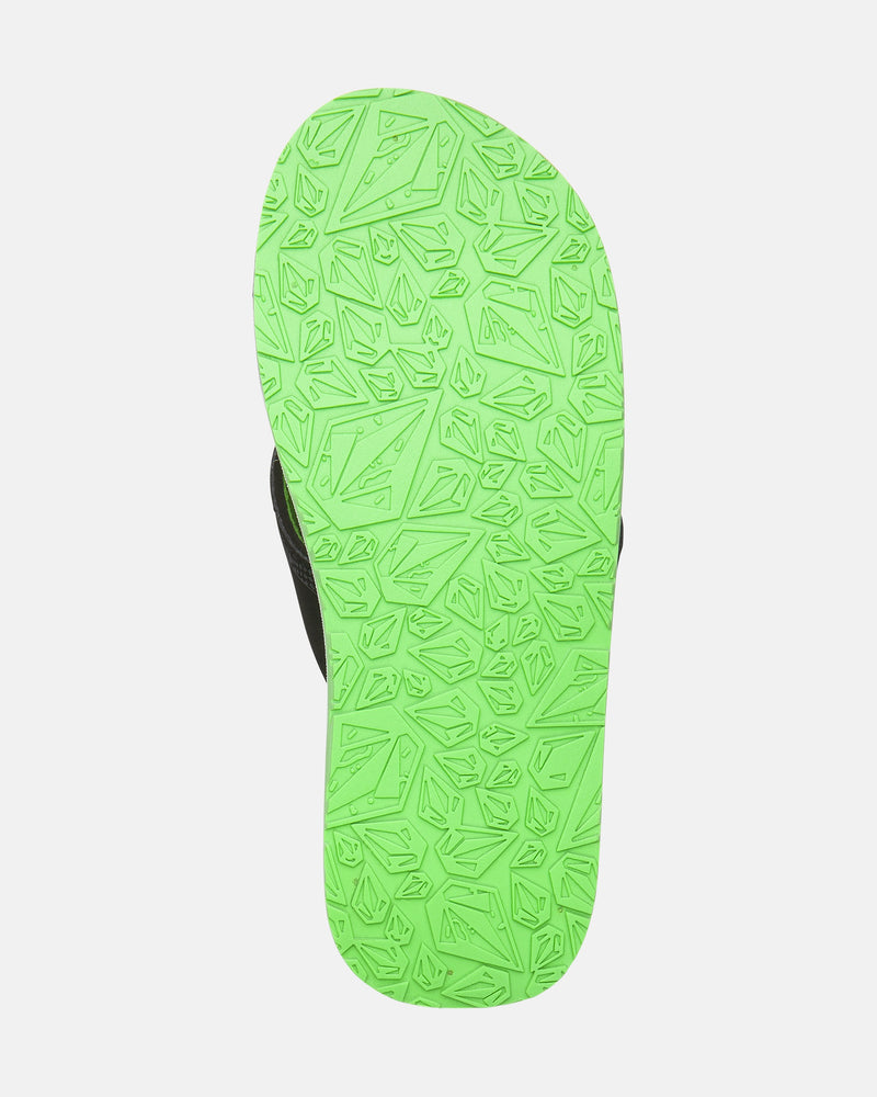 The image shows the bottom view of the Volcom Kids' Recliner 2 Big Youth sandal. It has a bright green sole with an irregular geometric pattern, a black strap, and a water-friendly design. Perfect for everyday adventures. White background.
