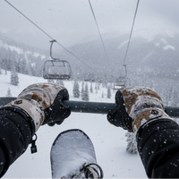 Person holding onto a ski lift pole with snow-covered gloves and skis, surrounded by a snowy landscape.