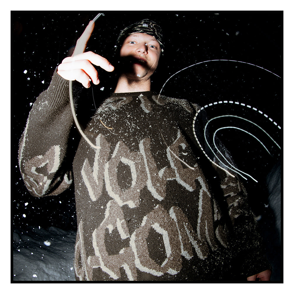 Person wearing a volcom sweater standing against a dark background and graphic swirls that give the illusion of snow.