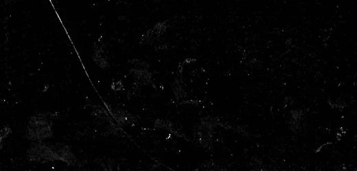 A black background with faint white specks and a thin, curved white line stretching from the top left corner toward the center, resembling scratches or dust on a dark surface.