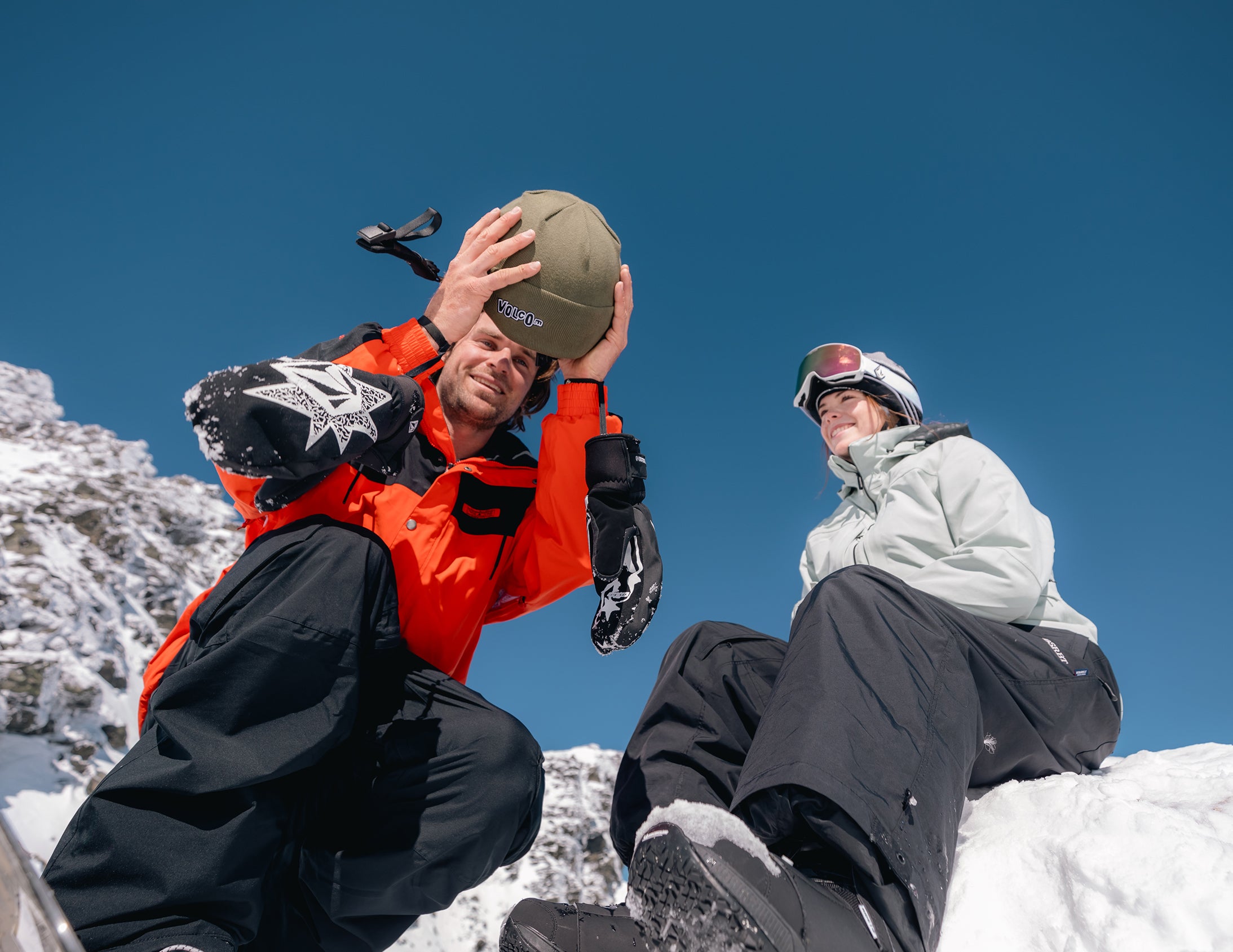 Two people sitting on a snowy ledge with clear blue sky