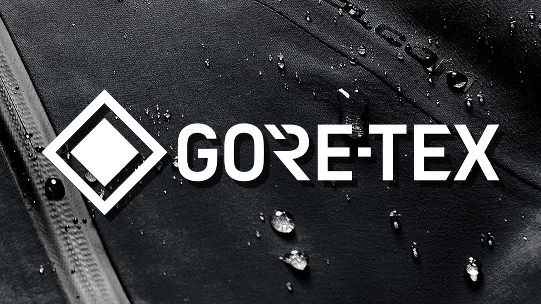 White GORE-TEX logo printed on a black waterproof fabric surface with water droplets, demonstrating the water-repellent property.