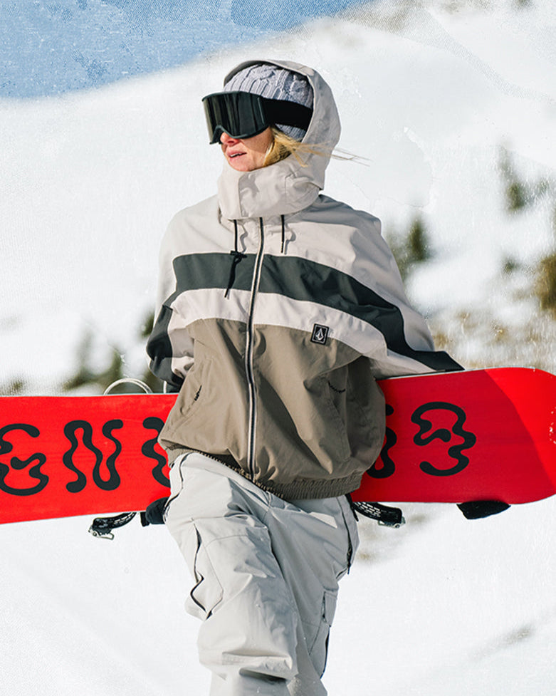 Person in winter gear holding a red snowboard with a mountainous background