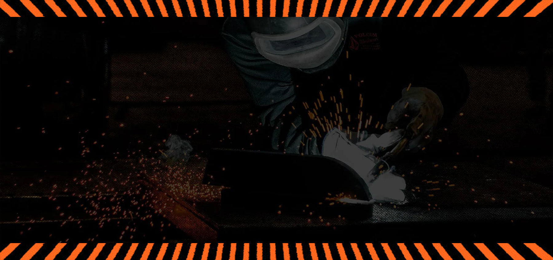 A person wearing protective gear welds metal, producing bright sparks and light. The image is framed with an orange and black striped border.
